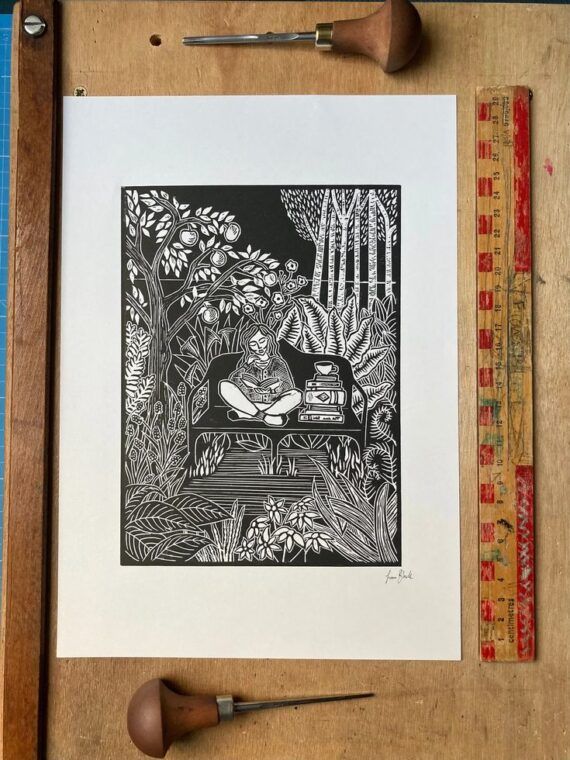 black and white lino print of a person sitting in a lush garden reading a book