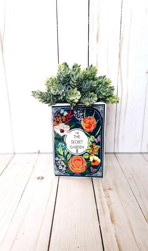 a book shaped vase with the cover of The Secret Garden in dark blue with bright flowers 