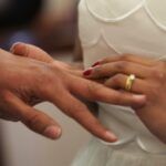 tan-skinned hands slipping on a wedding ring on another hand