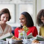 Black and white women eating, reading, and speaking with each other