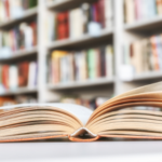 an open book on a table with bookshelves out of focus in the background