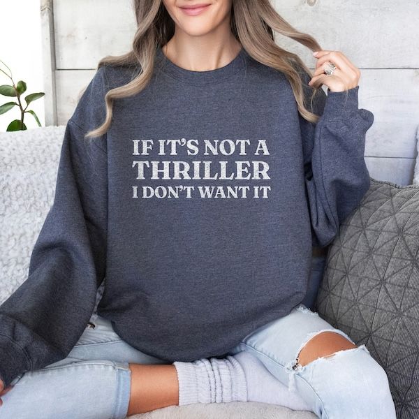 a woman wearing a charcoal grey sweater with white text that reads "If it's not a thriller, I don't want it"