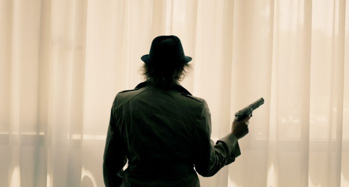 woman in a hat and trenchcoat holding a gun as seen from behind
