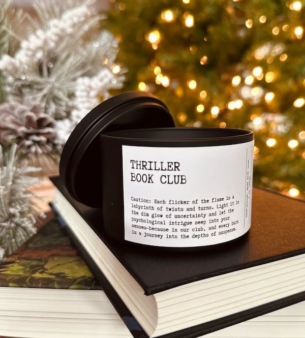 a candle resting on a black hardcover book. the candle label reads "thriller book club"
