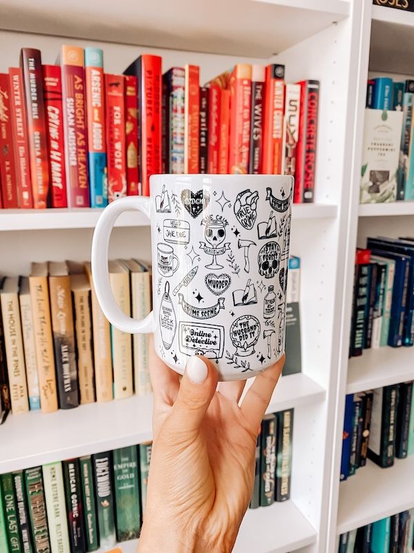 white coffee mug covered in mystery, thriller, and true-crime themed graphics and text, like a crystal ball with the words "the husband did it" inside and a skull with text that reads "stay out of the forest"