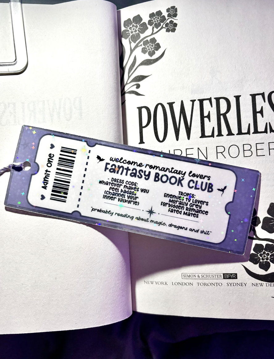 Image of a bookmark designed to look like a movie theatre ticket that says "fantasy book club" with a list of tropes, displayed on an open book