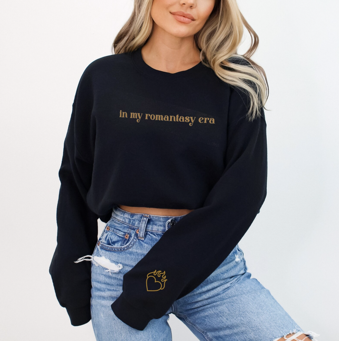 Image of the torso of someone wearing a black sweatshirt with "in my romantasy era" embroidered across the chest and a heart with flames on the sleeve