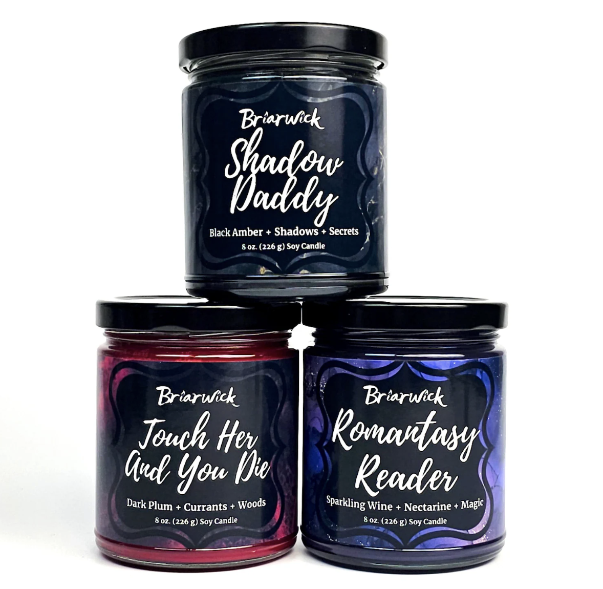An image of three candles in jars with labels reading "shadow daddy", "touch her and you die", and "romantasy reader"