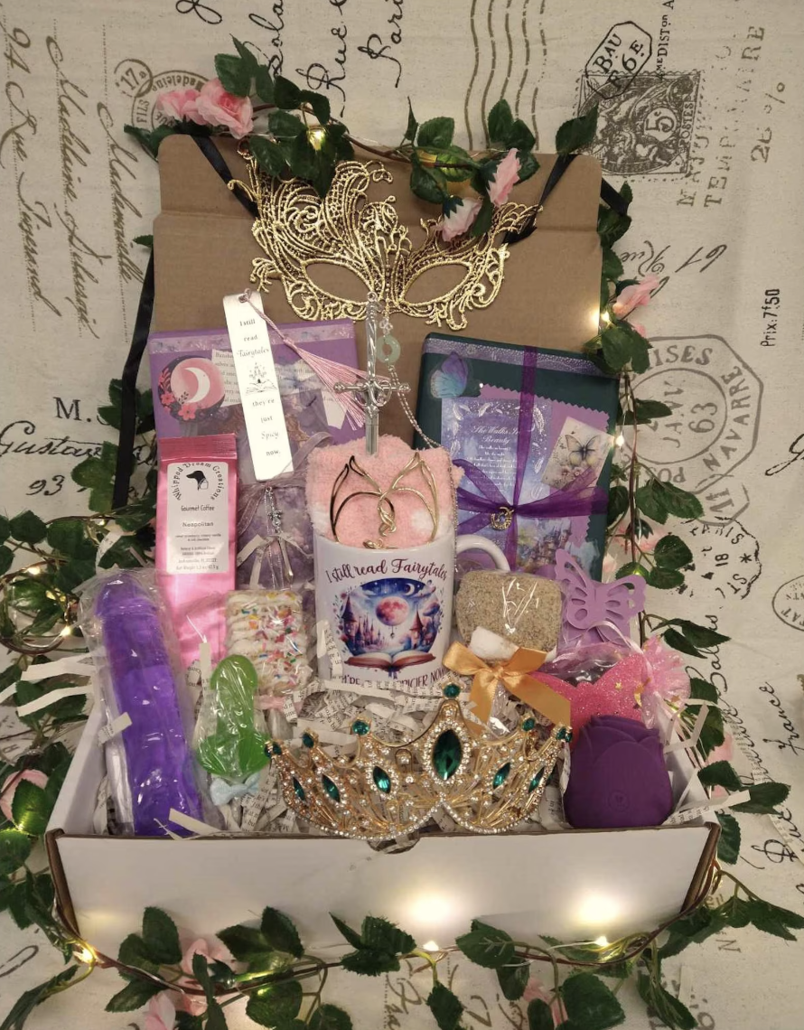 An image of an open box stuffed with romantasy goodies including wrapped mystery books, a crown, a mug, and mystery wrapped items