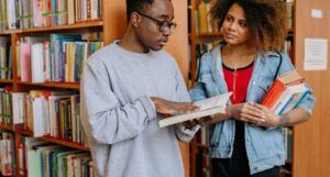 a dark brown-skinned Black man and a light brown-skinned Black woman reading with each other in a library