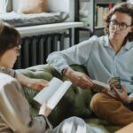 two people talking on a couch, both holding books