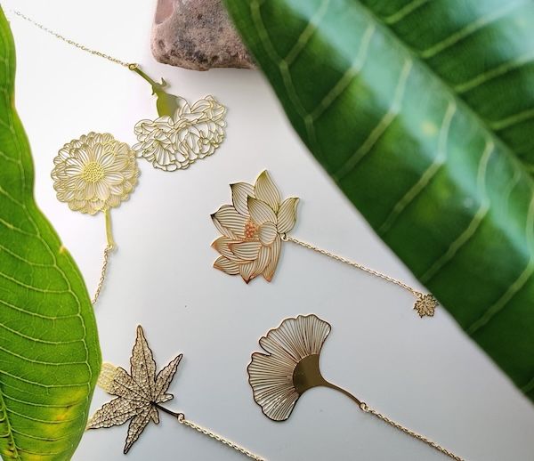 assortment of hollow metal floral bookmarks, including a marigold, dahlia, and a gingko leaf. each is gold in hue.