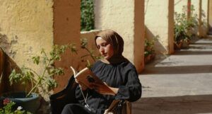 a light tan-skinned woman with a head scarf reading outside