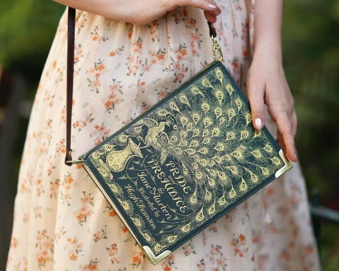 purse in the shape of a blue and gold vintage pride and prejudice book cover worn by a person wearing a light floral dress 