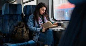 a woman reads on a train and drinks coffee