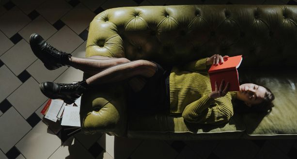 a fair-skinned woman laying down and reading on a couch