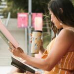 a light-skinned Asian woman reading a book on a pink bench