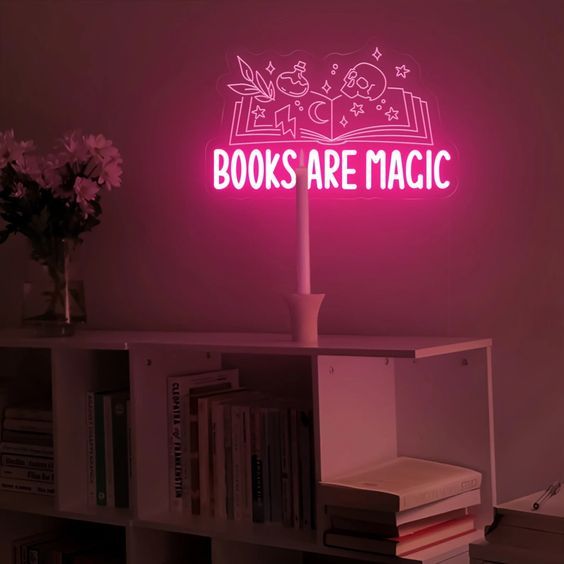 image of a dim room with a pink neon sign glowing the words Books Are Magic with an image flowers blooming from an open book