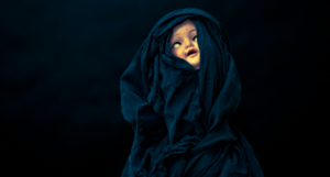 a creepy doll shrouded in black fabric against a black background