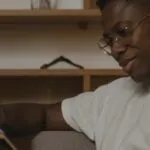 dark brown-skinned Black man smiling and reading a book