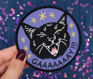 an embroidered patch of a cat winking and yowling with the word gaaay!! underneath
