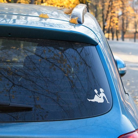 a blue car with the white silhouette of a girl reading as a sticker in the corner of the rear window.