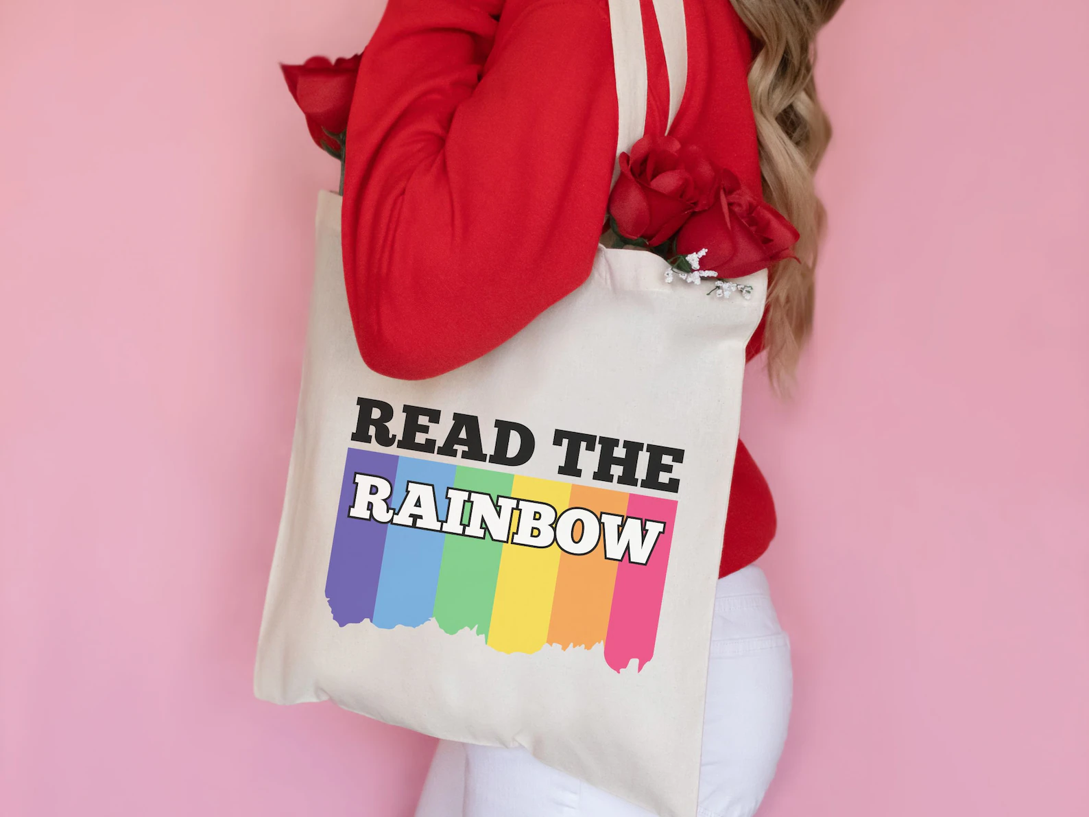 Image of a person holding a canvas tote bag. The bad has a rainbow on it with the words "read the rainbow."
