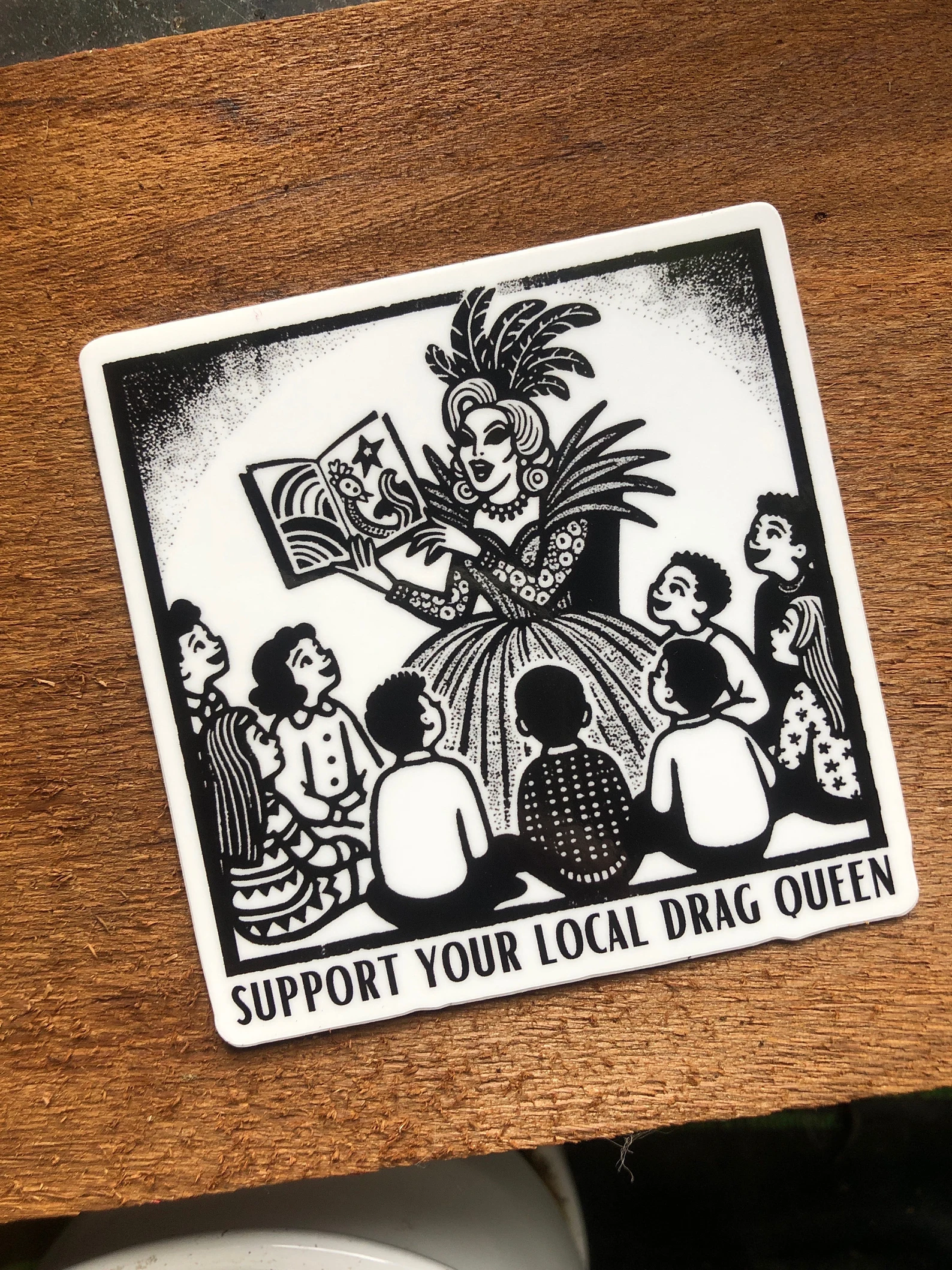 image of a black and white sticker featuring a drag queen reading a book to children. 