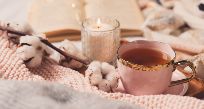 a mug of tea with a candle, cotton, fabric, and a book