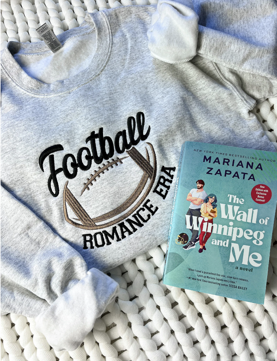 photo of a gray crewneck sweatshirt embroidered with a football and the text "football romance era" displayed next to the book The Wall of Winnipeg and Me