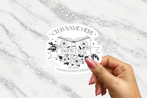 a white enamel sticker with a black graphic of an open book and text that reads "club name here"