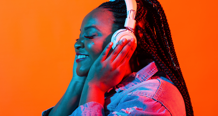 a photo of a young Black woman listening to headphones with a bright orange background