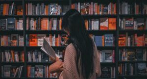 tan-skinned person with long black straight hair reading a book in front of a book store's shelves