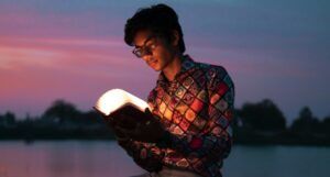 tan-skinned young man reading a book that is lighting up his face