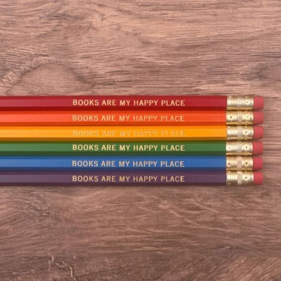 six pencils in the colors of the rainbow with gold print that reads books are my happy place