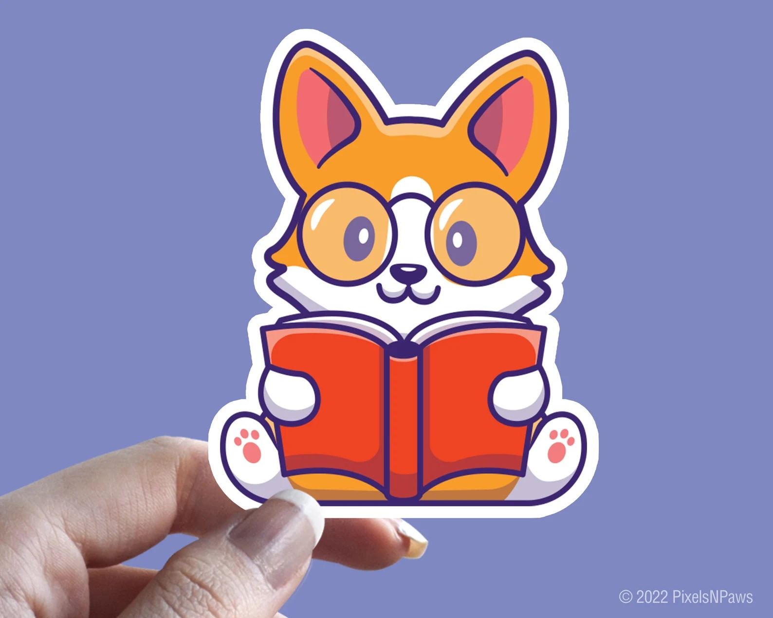 a photo of a sticker that features a red and white Corgi wearing glasses and reading a book