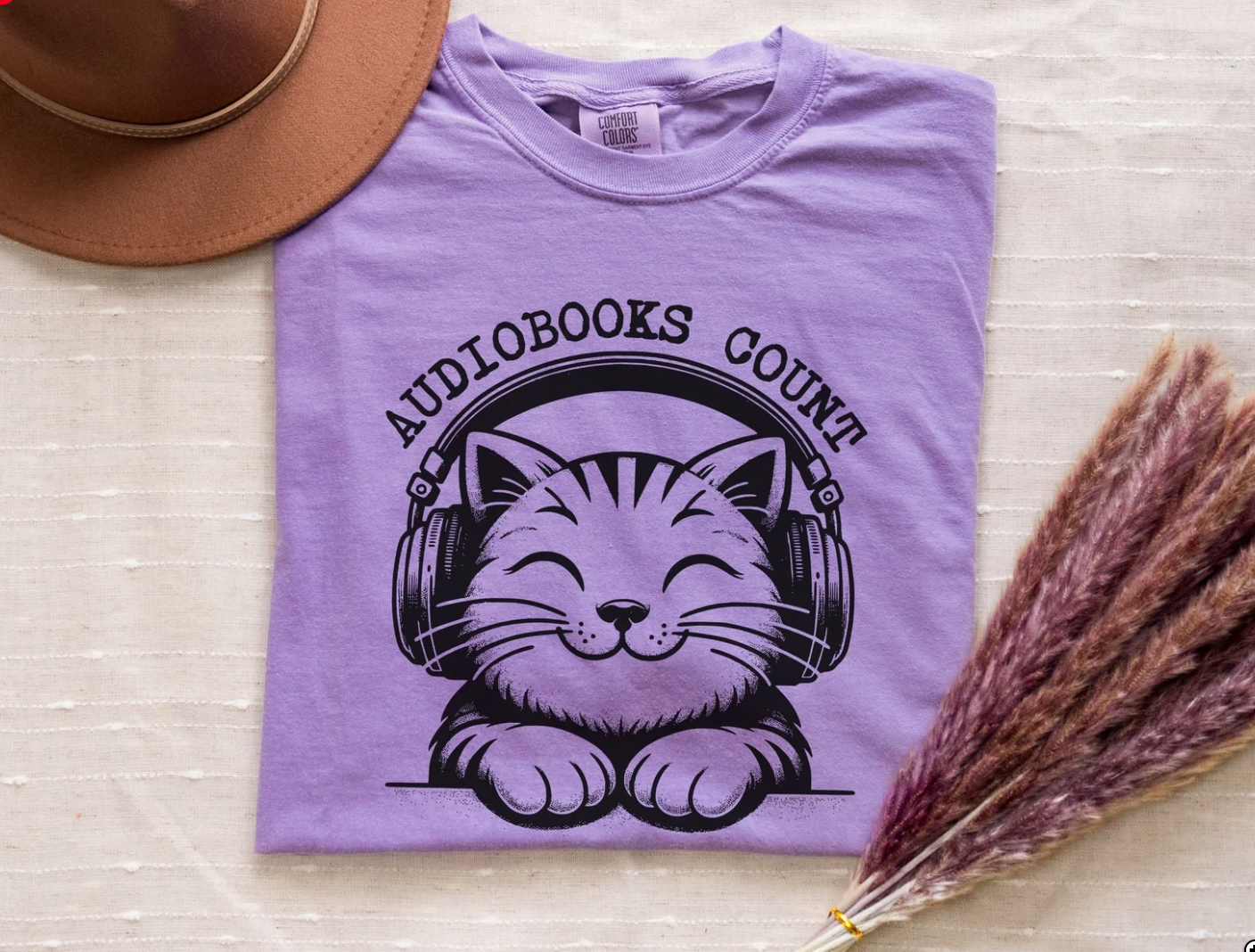 Image of a purple shirt with a cat wearing headphones on it. The text reads "audiobooks count."