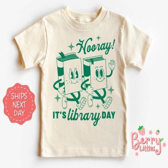 cream colored youth sized tshirt with retro lettering and an image of two books walking together. The text reads "hooray, it's library day!"