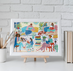 An art print of a colorfully illustrated scene with women of various races reading books on cozy chairs and cushions, surrounded by stacks of books as well as plants and a sleeping dog. 