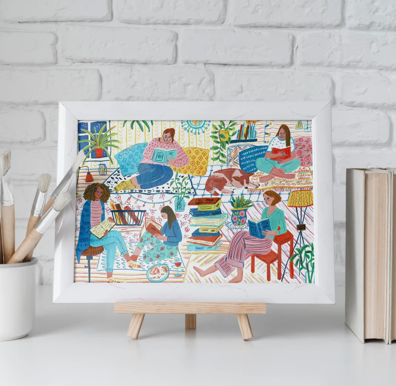 An art print of a colorfully illustrated scene with women of various races reading books on cozy chairs and cushions, surrounded by stacks of books as well as plants and a sleeping dog. 