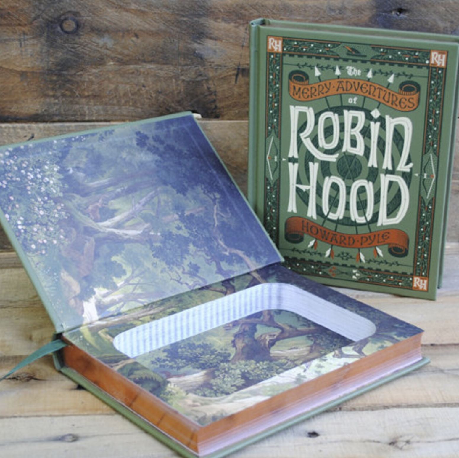Image of an open book with endpapers illustrated with forest imagery and carved out into a book safe. The closed version featuring the green cover of Robin Hood by Howard Pyle stands next to the open book.