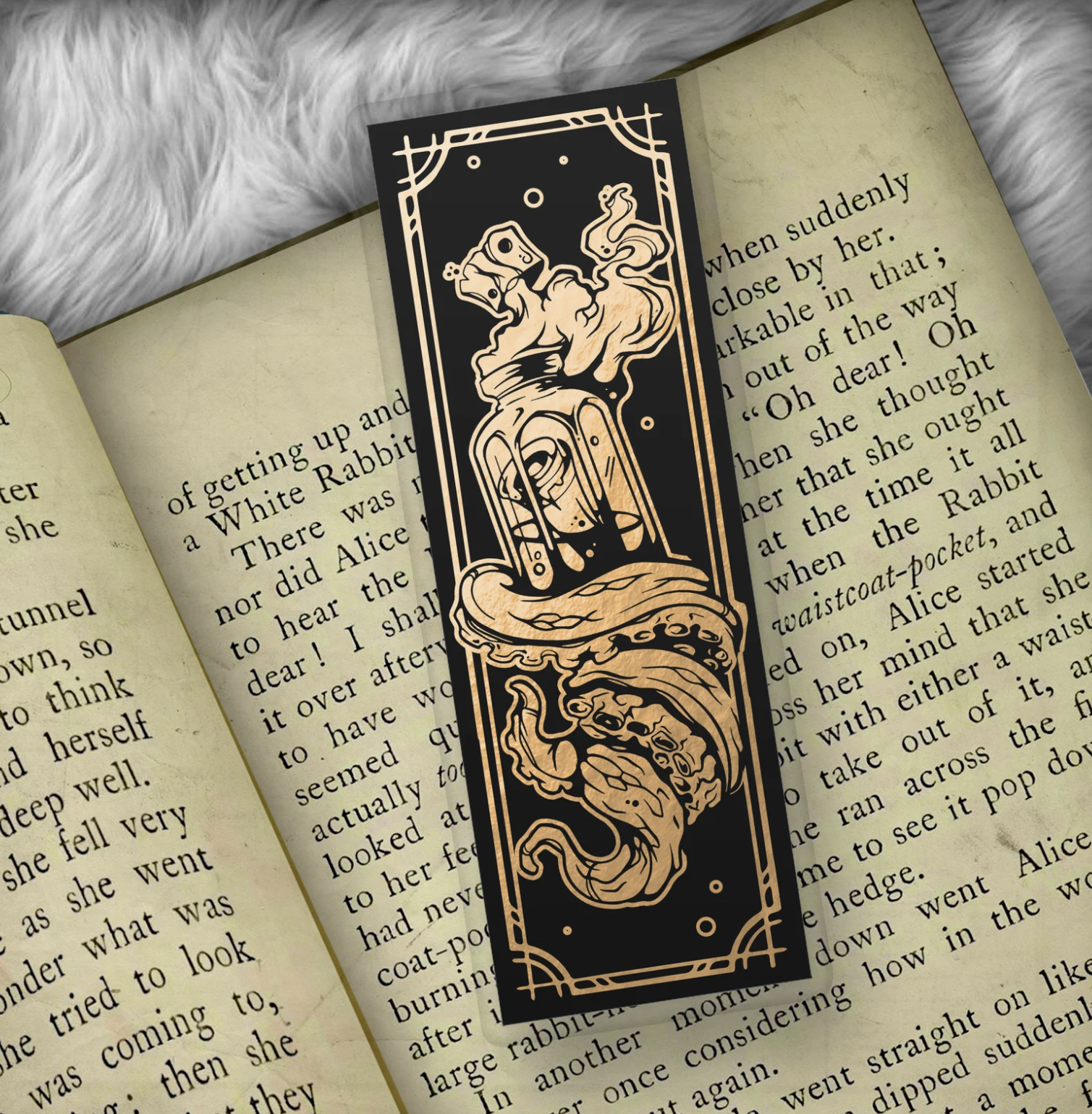 Black bookmark with a foil print of a message in a bottle with a tentacle wrapped around it laid against an open book.