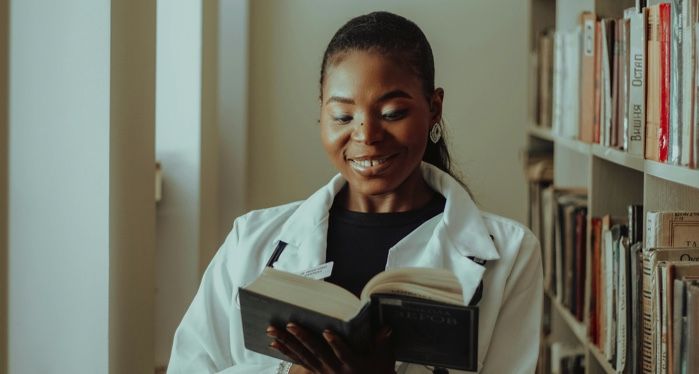 a brown-Skinned Black woman reading and smiling in a library
