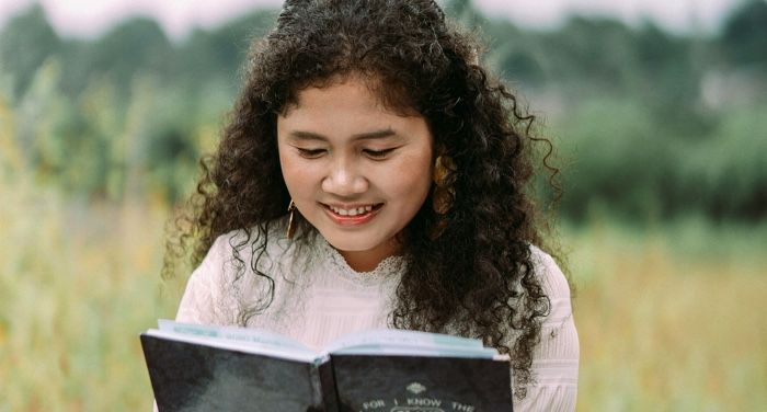 a fair-skinned woman of color reading a book in a field