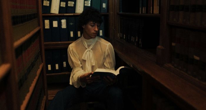 a lighter-skinned masc presenting person reading a book in a dark corner of a library