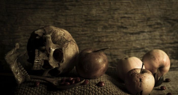 a skull, apples, and candies arranged on a mat in sepia tones