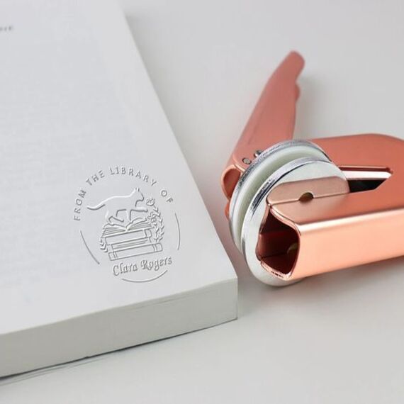 Image of a white page with an embossed circle and personalization next to a rose gold embosser