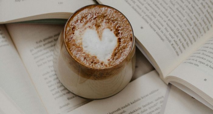 latte with heart-shaped foam in a mug surrounded by books