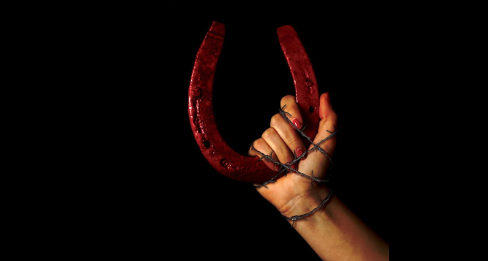 cropped cover of The Unmothers showing a hand wrapped in barbed wire holding a bloody horseshoe