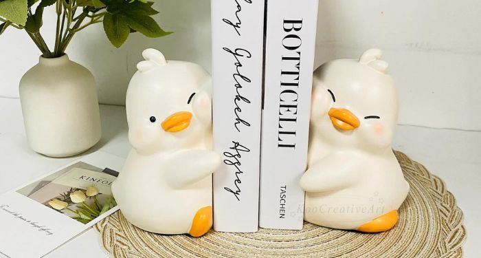 a set of bookends on either side of three books. the bookends are small white chubby ducklings